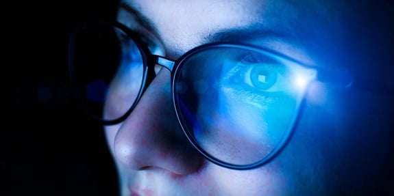 Woman with glasses where blue light is reflected in the lens