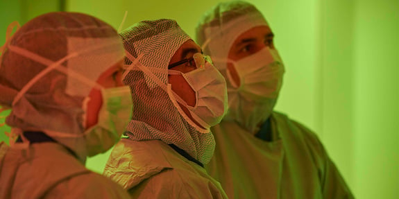 Kirurgen och sjukvårdspersonalen med uniform och munskydd tittar på skärmen.