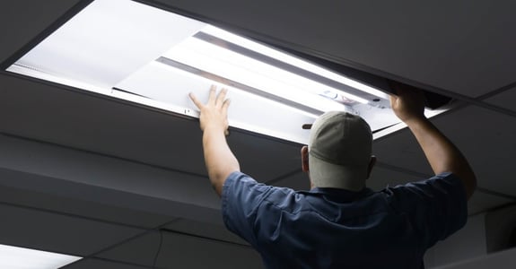 Man with backwards cap and blue t-shirt changes fluorescent tube in a ceiling lamp