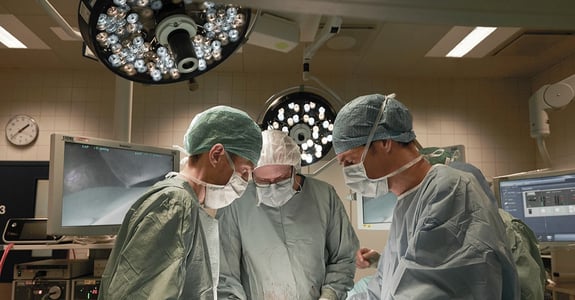Tre kirurger under åben operation under hvidt lys 