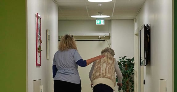 Medarbejder og borger går sammen på gangen på et plejehjem med Chromavisos døgnrytmelys