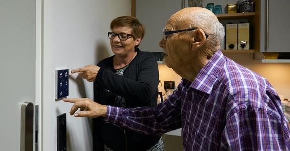 Plejehjemsleder hjælper ældre borger med at anvende betjeningspanelet til døgnrytmelyset fra Chromaviso
