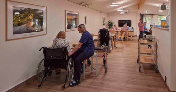 Social- og sundhedsassistent sidder og hjælper en ældre dame i kørestol med at spise