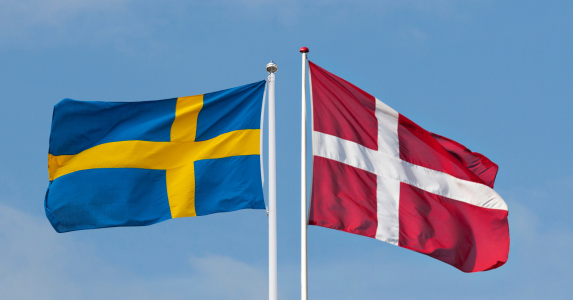 A Swedish and a Danish flag are blowing in the wind on a clear blue sky